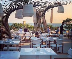 an outdoor dining area overlooking the ocean with white tables and chairs set up for people to eat