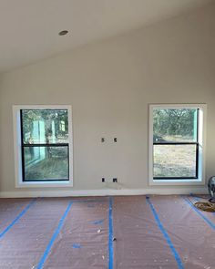 an empty room with two windows and some blue tape on the floor in front of them