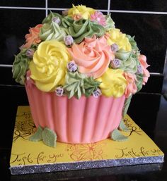 a pink cupcake decorated with flowers on top of a yellow cake plate next to a black tile wall