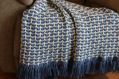 a blue and white blanket sitting on top of a couch next to a brown chair