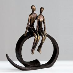 a bronze sculpture of two people sitting on top of a circular object with their hands together