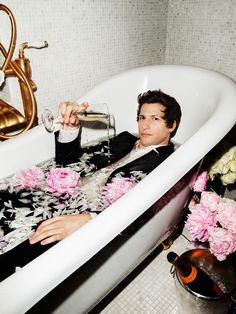 a man sitting in a bathtub drinking from a wine glass with pink flowers on the floor