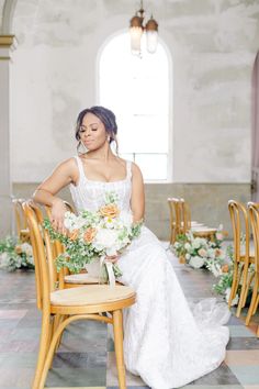 a bride sitting on a chair with flowers in her hair and holding a flower bouquet