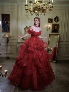 a woman in a red dress standing next to a chandelier