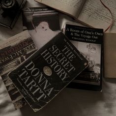 several books laying on top of a bed next to an open book with the title's secret history written in it