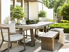 an outdoor table and bench with potted trees in the background