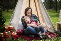 a woman and child sitting in front of a teepee with presents on the ground