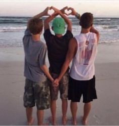 three boys standing on the beach holding hands in the shape of a heart with their hands