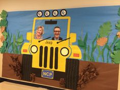 a man and woman are sitting in a jeep made out of paper mache on the side of a wall