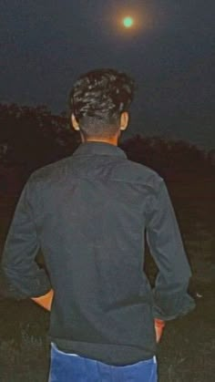 a man standing in the grass at night with his back turned to the camera, looking into the distance