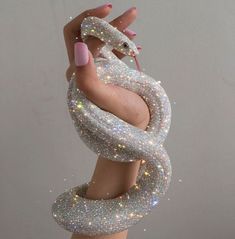 a woman's hand holding up a silver snake sculpture with glitter on the skin