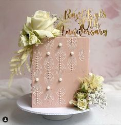 a pink cake with white flowers and gold lettering on top is sitting on a plate