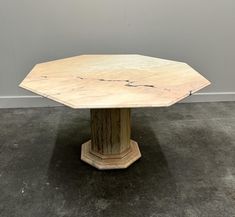 an octagonal marble dining table with hexagonal pedestals on the top, in front of a white wall