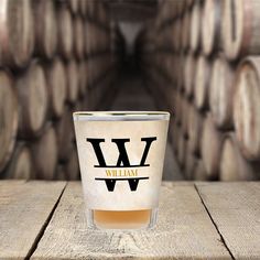 a shot glass sitting on top of a wooden table next to stacks of wine barrels