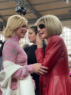 two women standing next to each other in front of a crowd at a fashion show