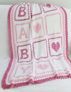 a crocheted blanket with letters and hearts on it, next to a teddy bear