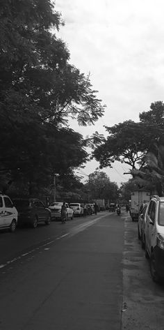 black and white photograph of cars parked on the side of a road with trees in the background