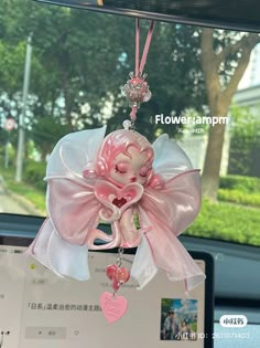 a pink teddy bear hanging from the front of a car with a heart charm attached to it