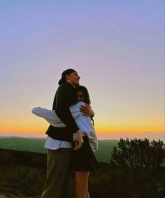 a man and woman hugging each other on top of a hill