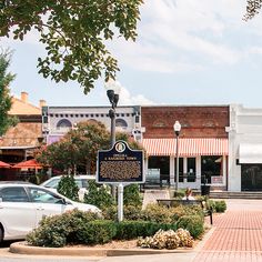 a small town square with cars parked on the side walk and shops in the background