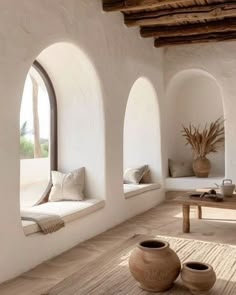 a living room with white walls and arched windows on the wall is filled with potted plants