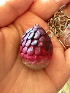 a hand holding a small red and purple object in it's left hand with a chain attached to it