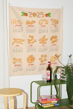 a wall hanging with a calendar on it next to two small tables and a plant