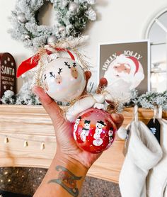 a hand holding two ornaments in front of a fireplace