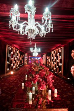 a long red carpeted hall with chandeliers and flowers on the floor, lit by candles