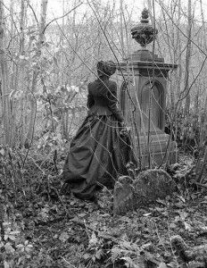 black and white photograph of a woman in an old fashioned dress standing next to a grave