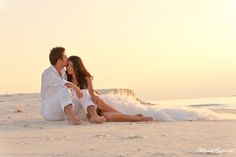 a man and woman are sitting on the sand at the beach with their arms around each other