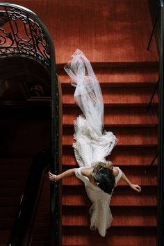 a woman in a white dress is walking down the stairs with her arms spread out