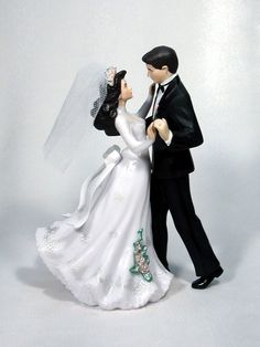 a bride and groom figurine standing next to each other on a white background