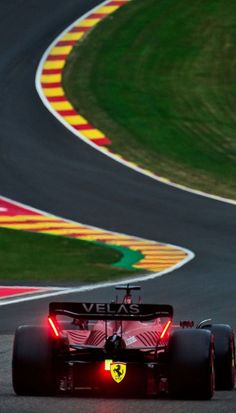 a red race car driving on a track with grass and yellow stripes around it's tires