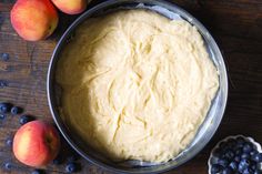 a pan filled with batter next to blueberries and peaches on a wooden table