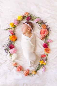 a baby is laying down in a flower circle on a white sheet with pink, yellow and orange flowers around it