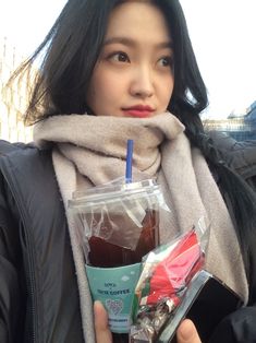 a woman is holding a cup and some food in her hand while wearing a scarf