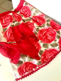 a red scarf is laying on the floor next to a white tablecloth with roses