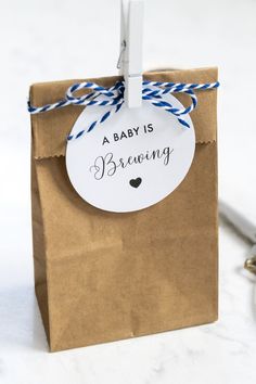 a baby is brewing gift bag with twine on the handle and tag that says, a baby is brewing