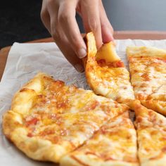 a person taking a slice of pizza from a pan on a table with white paper