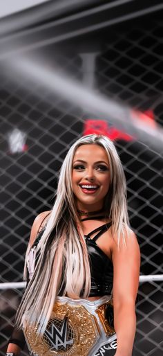 a woman in a wrestling outfit standing next to a metal cage with a smile on her face