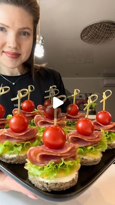 a woman is holding a tray with sandwiches and tomatoes on it, while smiling at the camera