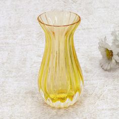 a yellow glass vase sitting on top of a table next to a white and gray flower