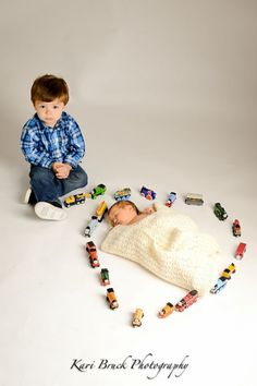 a young boy sitting on the floor surrounded by toy cars and toys in front of him