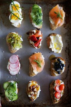 an assortment of small sandwiches with different toppings on them sitting on a baking sheet