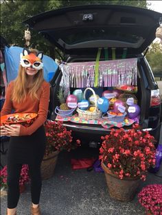 a woman standing in front of a trunk filled with food and glasses on top of her head