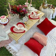 the table is set with red and white plates, napkins, and pink flowers