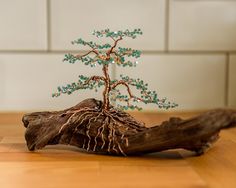 a small tree with green and blue beads sitting on top of a piece of wood