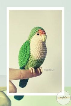 a crocheted green and white bird perched on a hand held by someone's finger