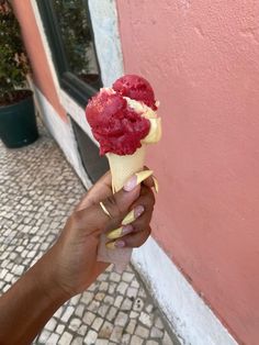 a hand holding an ice cream cone with raspberries on it, in front of a pink wall